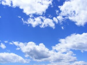 A bright blue sky filled with fluffy white and light gray cumulus clouds scattered across the frame, with patches of clear blue sky visible between the cloud formations.