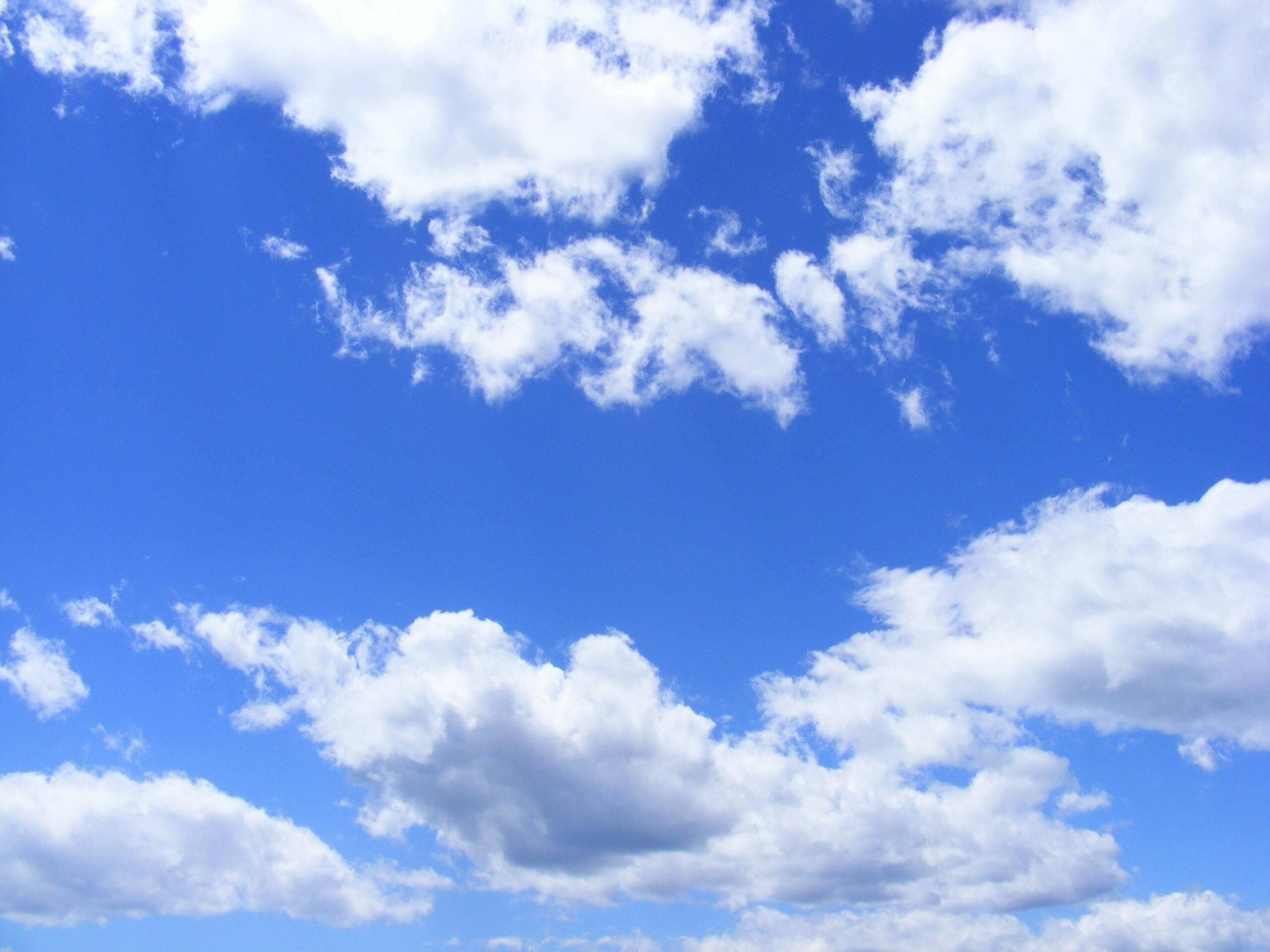 A bright blue sky filled with fluffy white and light gray cumulus clouds scattered across the frame, with patches of clear blue sky visible between the cloud formations.