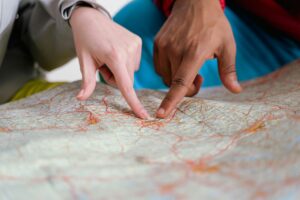 Two people's hands pointing at specific locations on a detailed map with colorful route markings, collaboratively planning or discussing directions and destinations